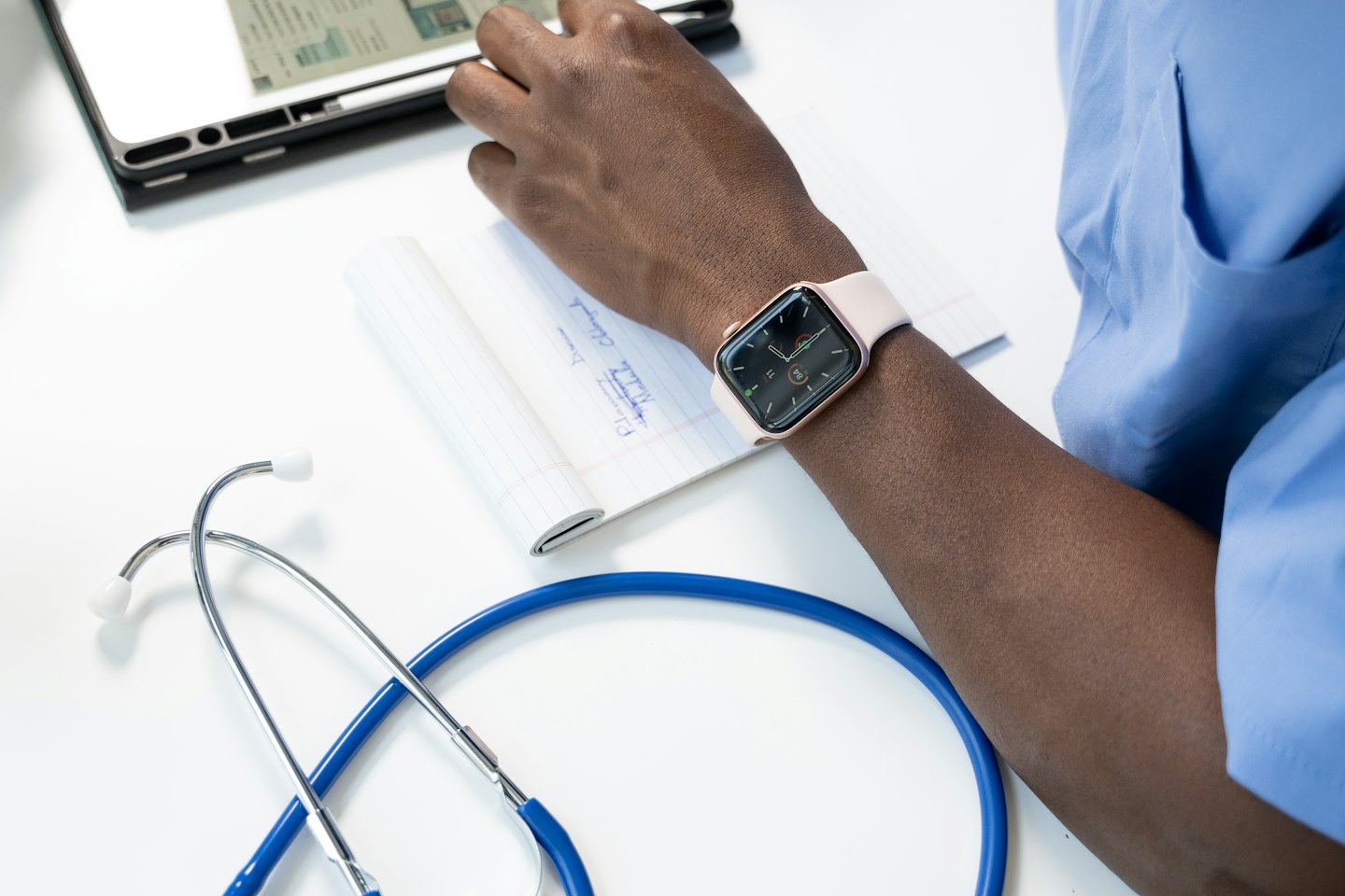 Medical professional writing notes with a stethoscope and tablet.