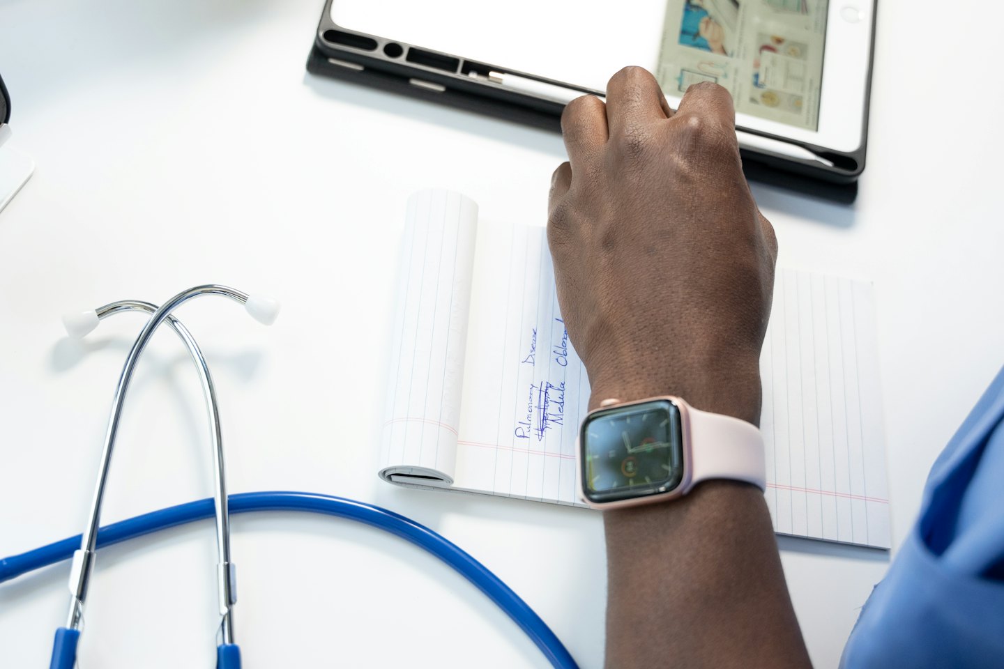 Medical professional's hands using a tablet and writing in a notebook.