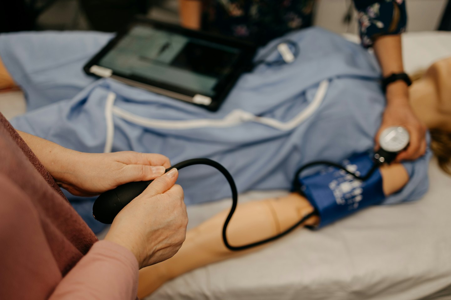 Hands operate a blood pressure cuff on a medical manikin.